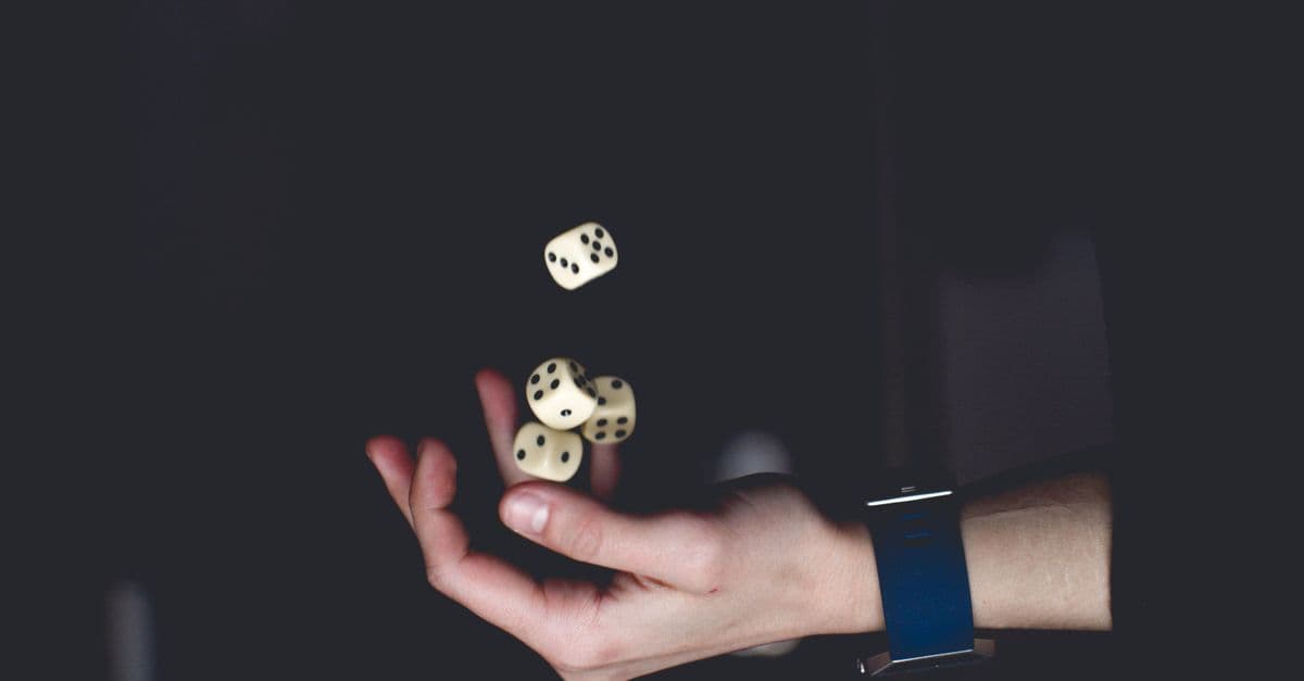 A close-up of a hand tossing several dice against a dark background, symbolizing chance and luck.