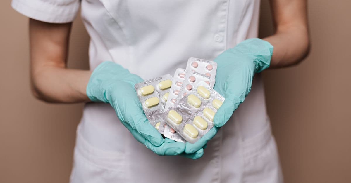 A healthcare professional in gloves and uniform holding blister packs of pills, showcasing medical care.