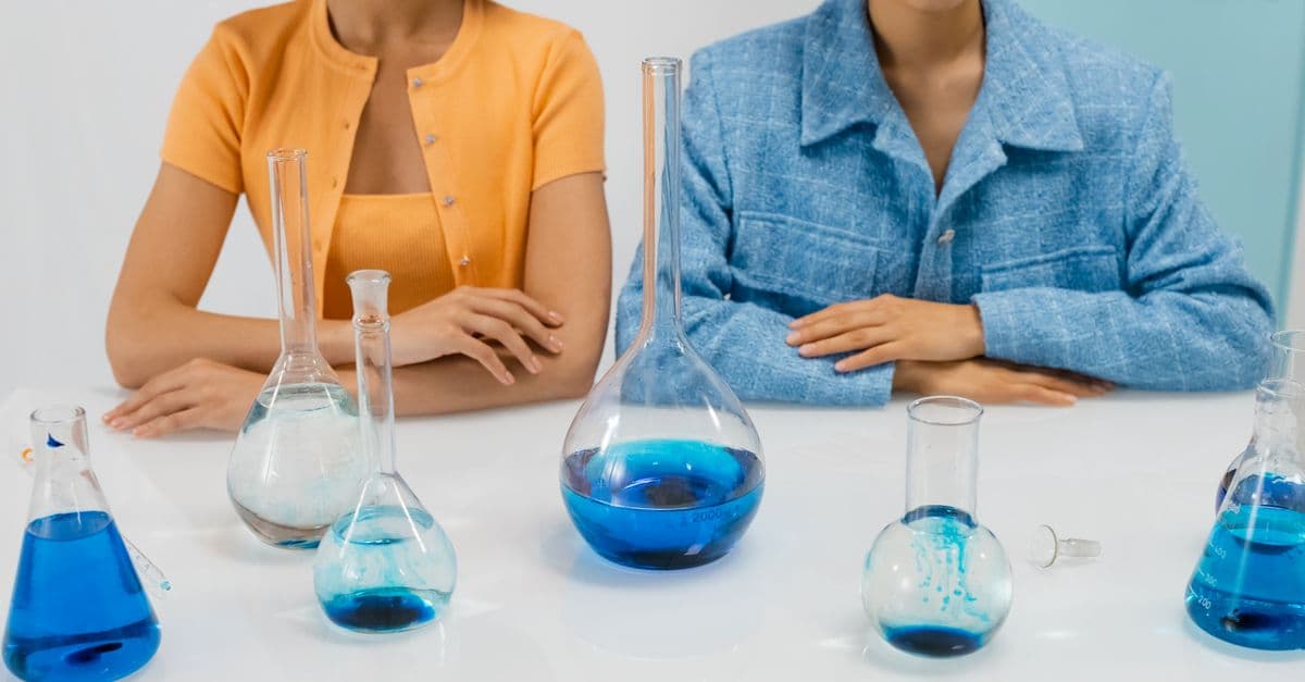Two women scientists in a lab with flasks conducting an experiment using blue liquid.