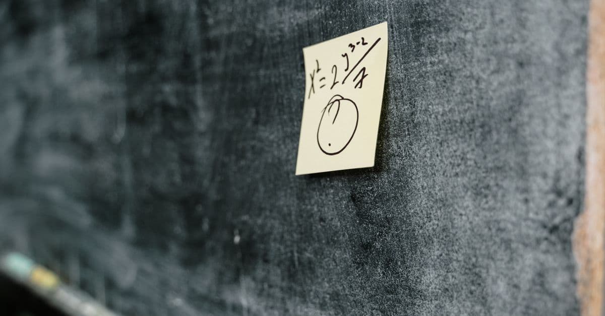 Close-up of a blackboard with a sticky note displaying a handwritten equation and drawing.