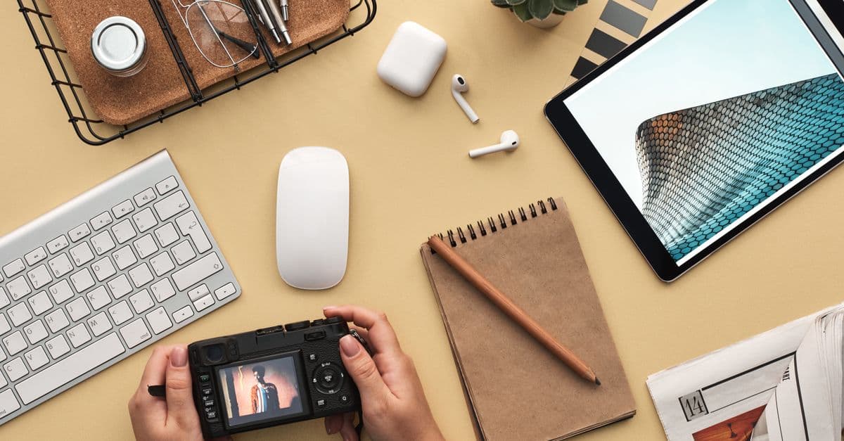 Overhead view of a modern workspace featuring tech gadgets, a camera, and a notepad.