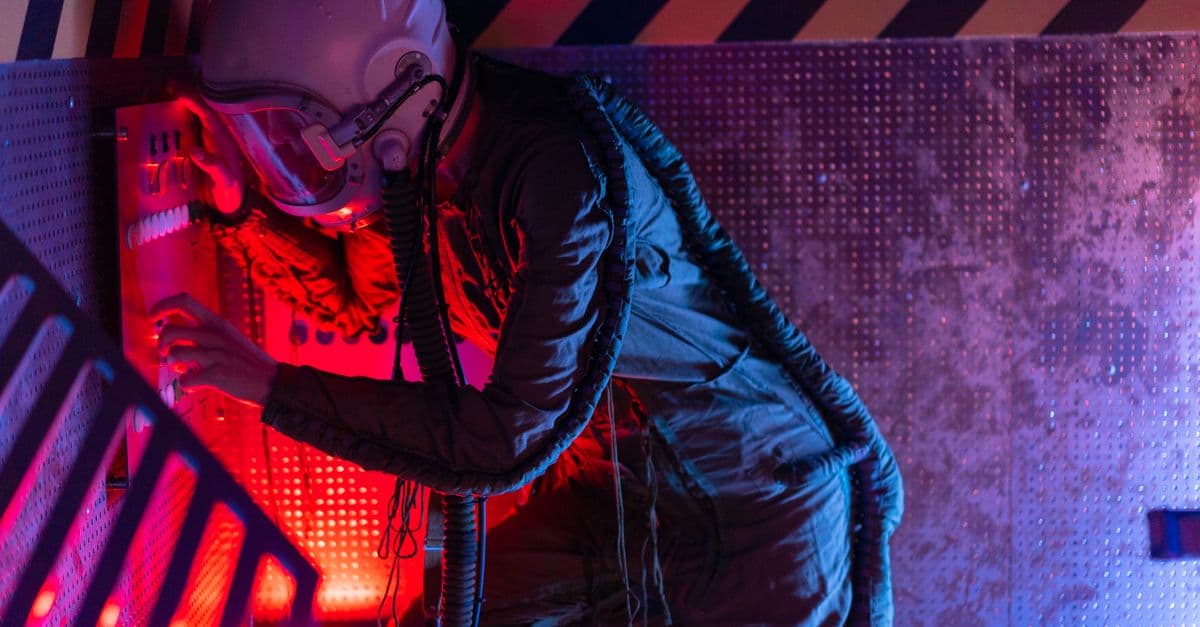 A woman in a spacesuit operates a futuristic control panel, bathed in vibrant red and blue lights.