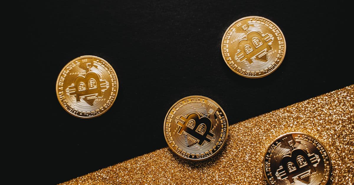 Stylish arrangement of golden Bitcoin coins on a sparkling gold glitter and black background.