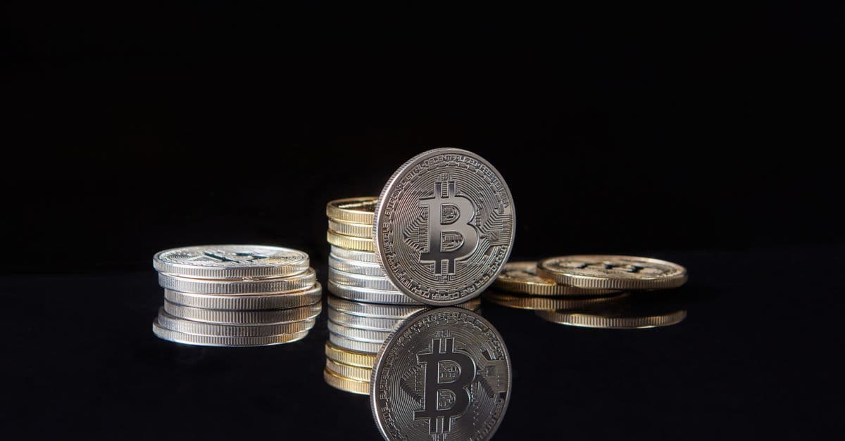 Silver bitcoins on a reflective surface beside a dark network pattern, representing digital-asset compliance infrastructure.
