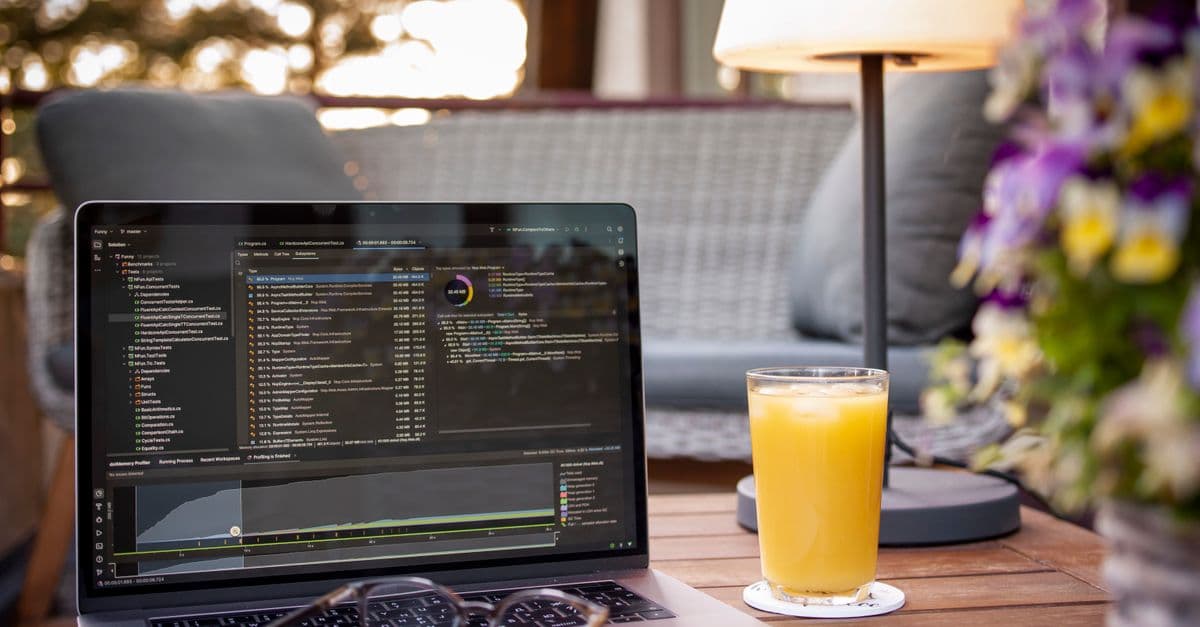 Laptop displaying code on a balcony with orange juice and flowers, under ambient light, perfect for work-from-home settings.
