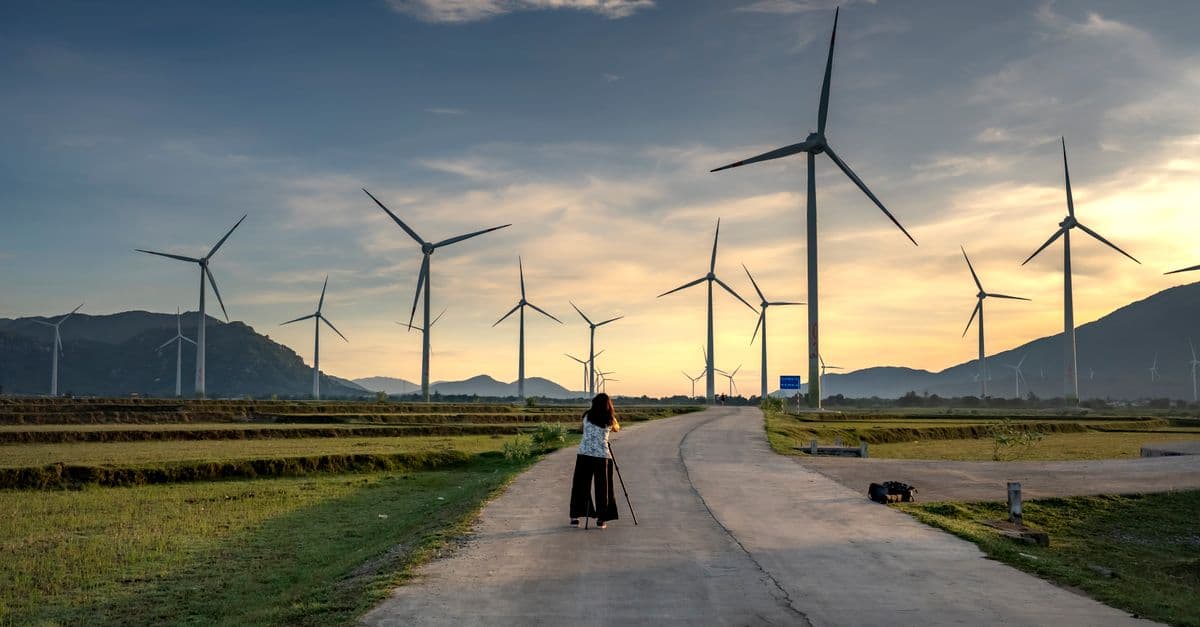 A scenic view of a wind farm at sunrise, featuring a photographer capturing the scene.