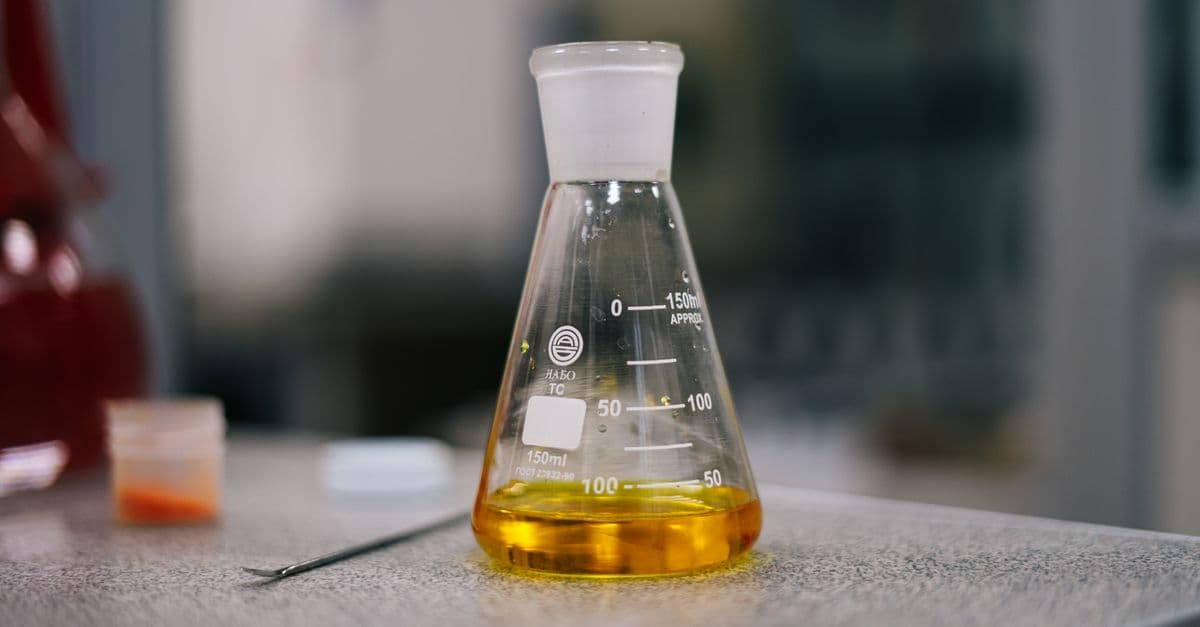 Close-up of an Erlenmeyer flask with yellow liquid in a laboratory setting.
