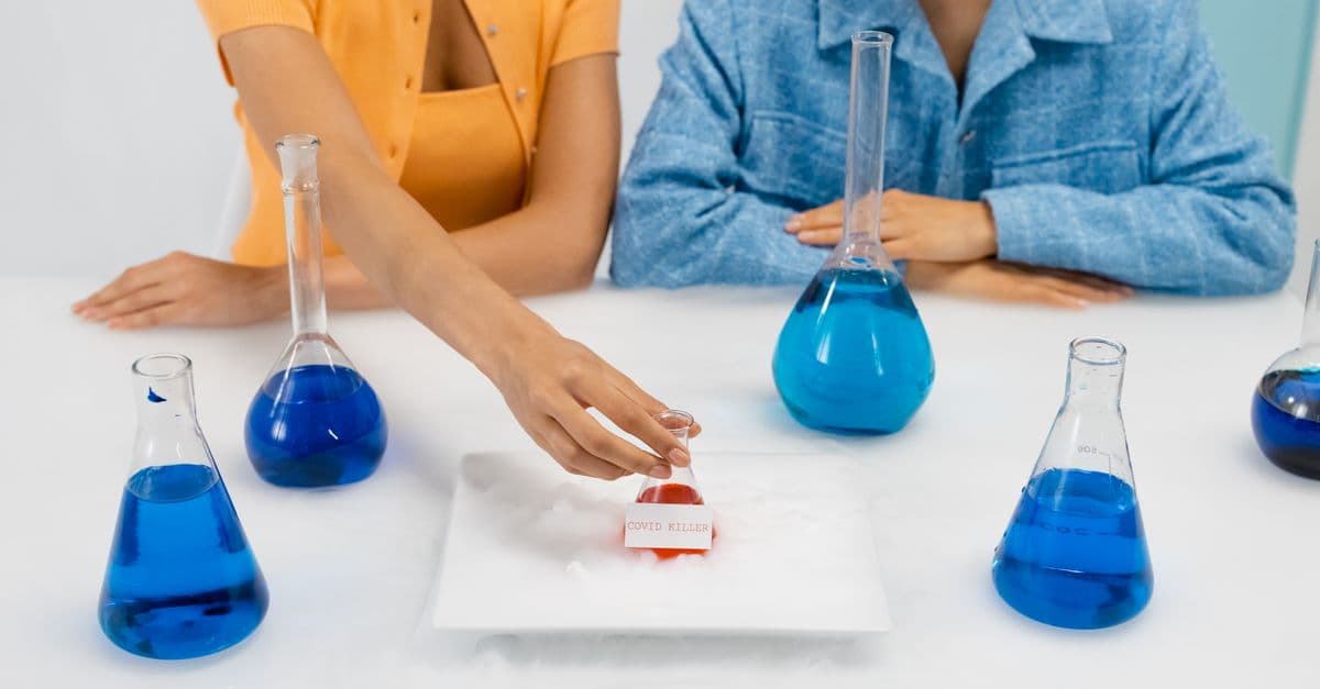 Two women in a laboratory setting conducting an experiment, using Erlenmeyer flasks containing blue liquid.