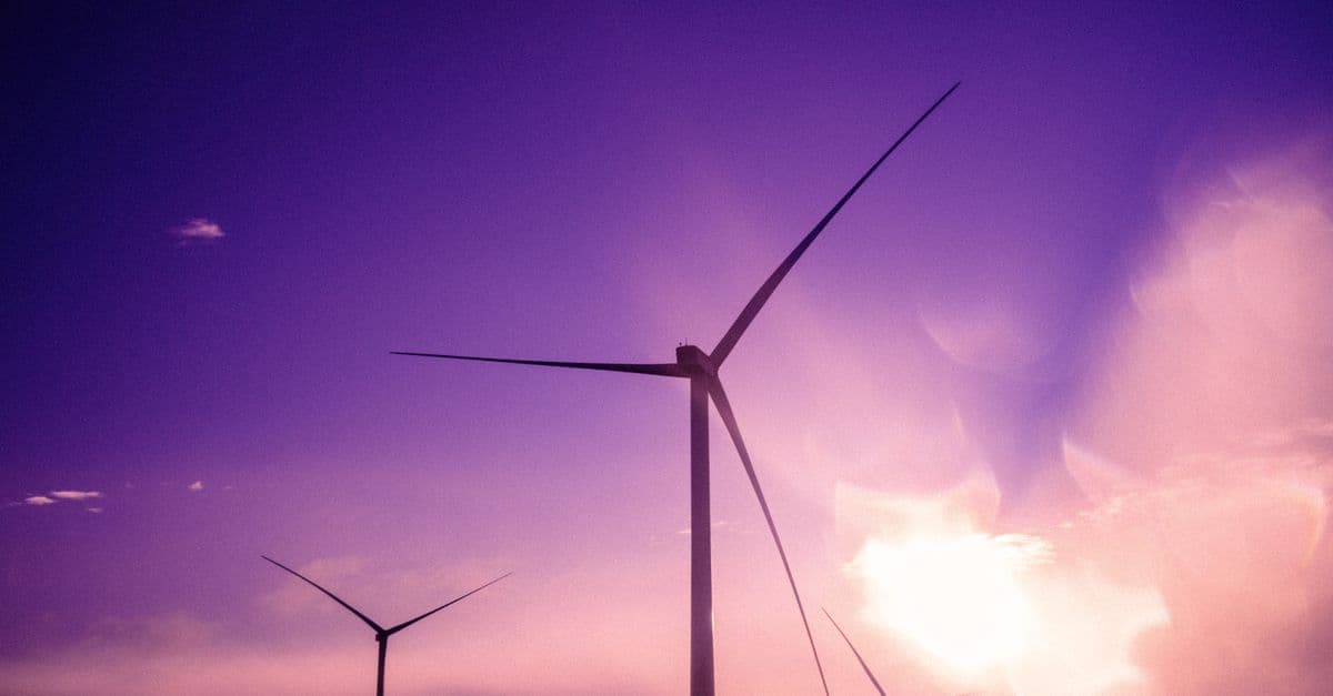 Three wind turbines silhouetted against a purple sunset sky, embodying renewable energy.