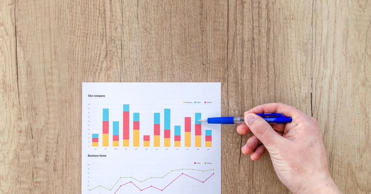 A hand points a pen at business graphs on a wooden table, highlighting data analysis.
