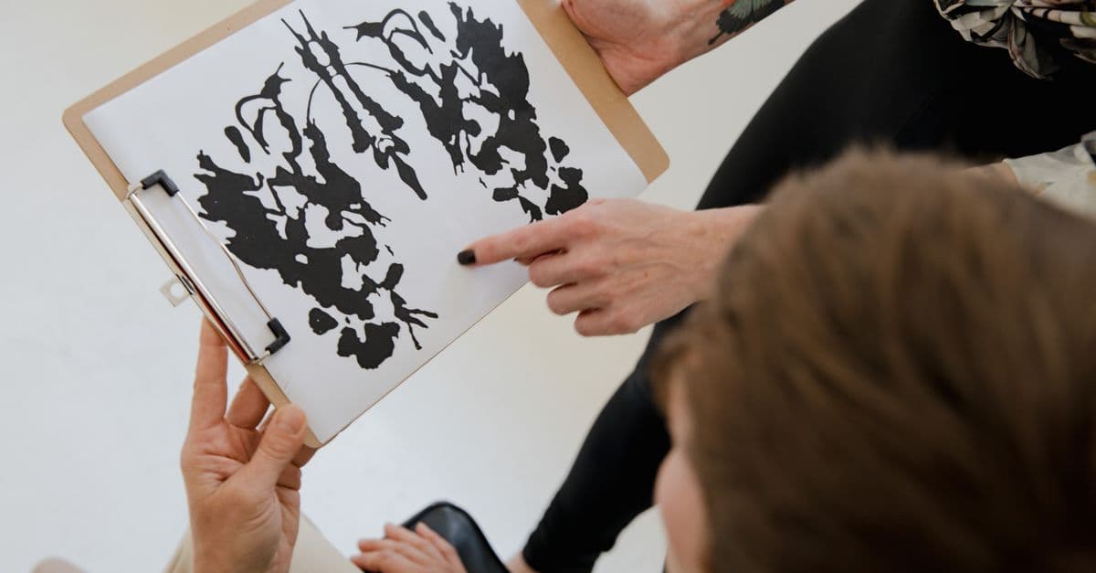 Hands holding a clipboard with an inkblot for psychological analysis.