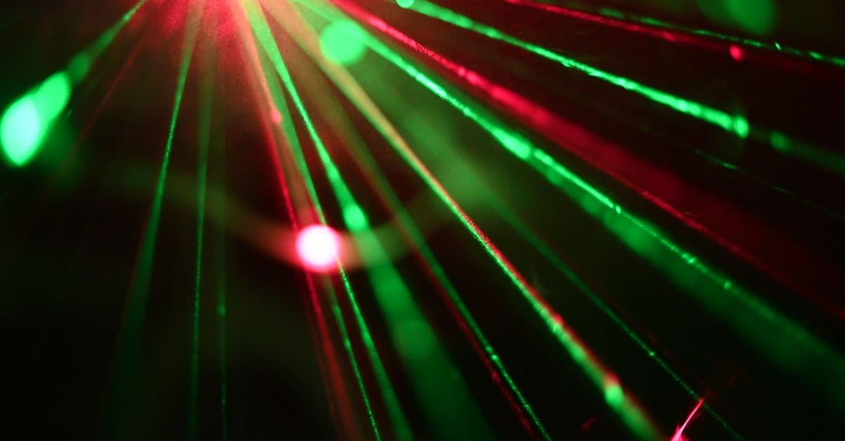 Dynamic display of red and green laser lights creating vivid rays across a dark background.