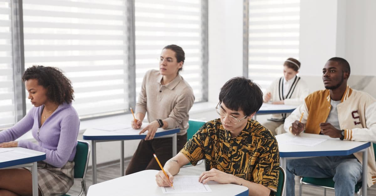 A diverse group of students writing exam papers in a well-lit classroom environment.