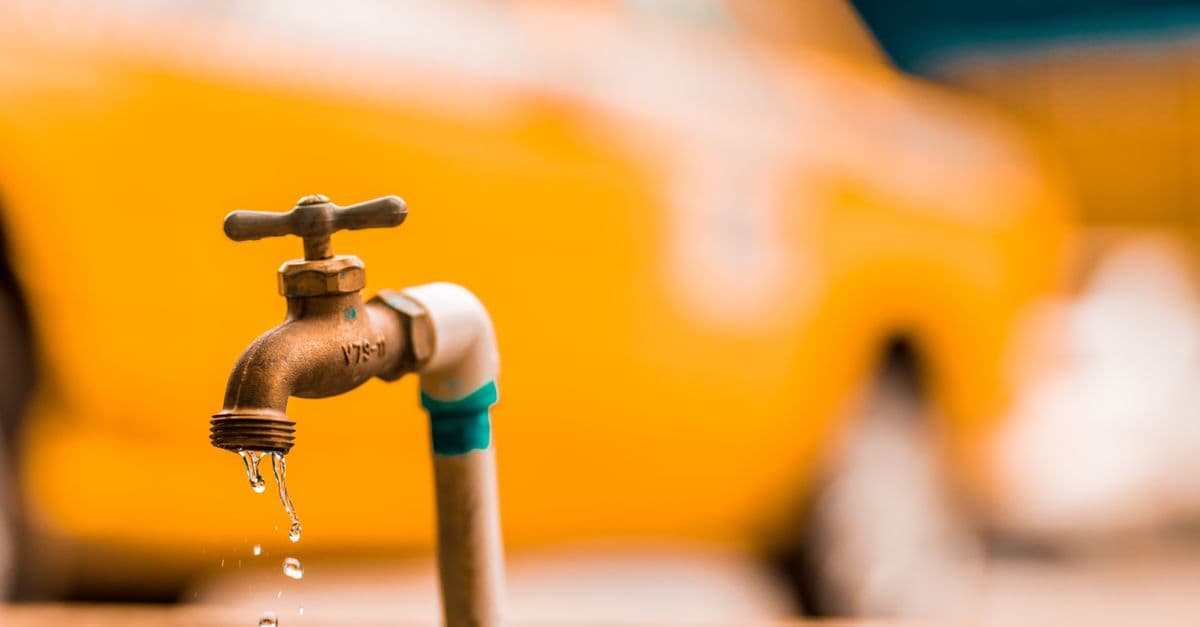 Macro shot of a brass faucet with water droplets against a blurred yellow background.