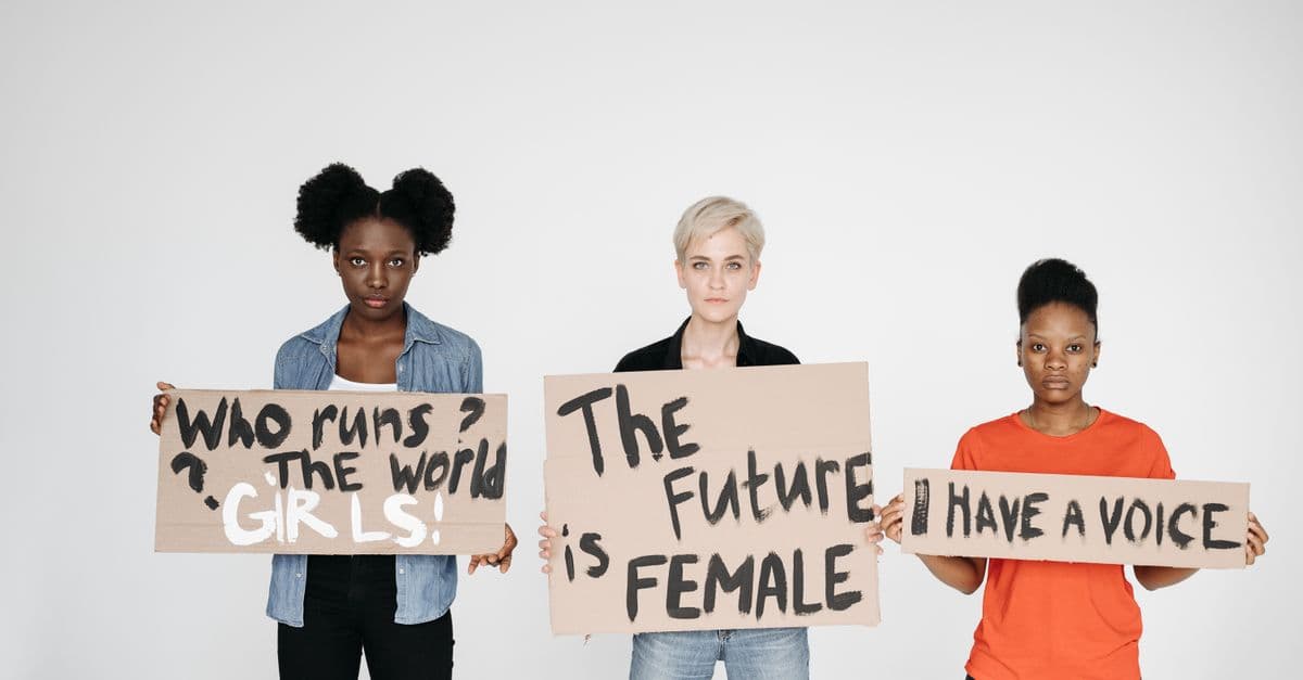 Three diverse women holding signs empowering female voices and rights.