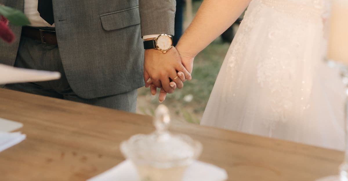 A close-up photo of a bride and groom holding hands during a wedding ceremony.