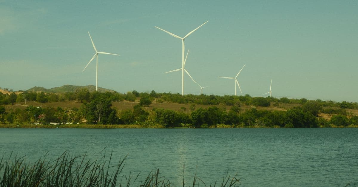 Stunning view of wind turbines on a hilltop overlooking a serene lake in Mui Ne, Vietnam.