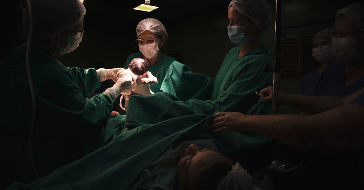 A medical team assists a childbirth in a dimly lit hospital operating room.