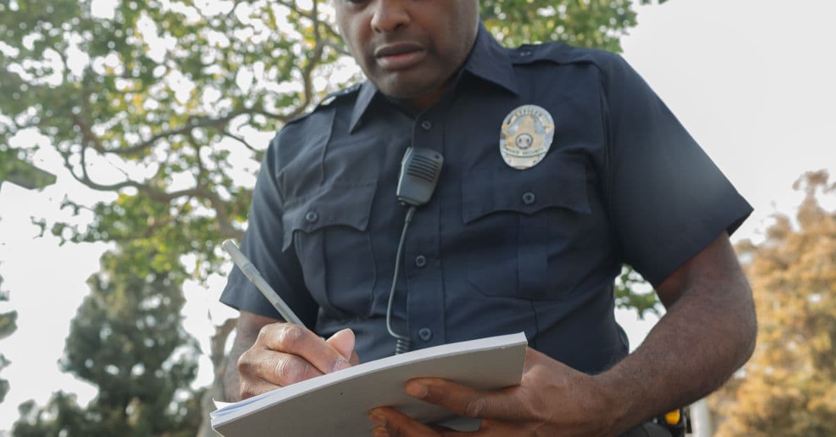 A focused police officer writes a ticket outdoors during the day.