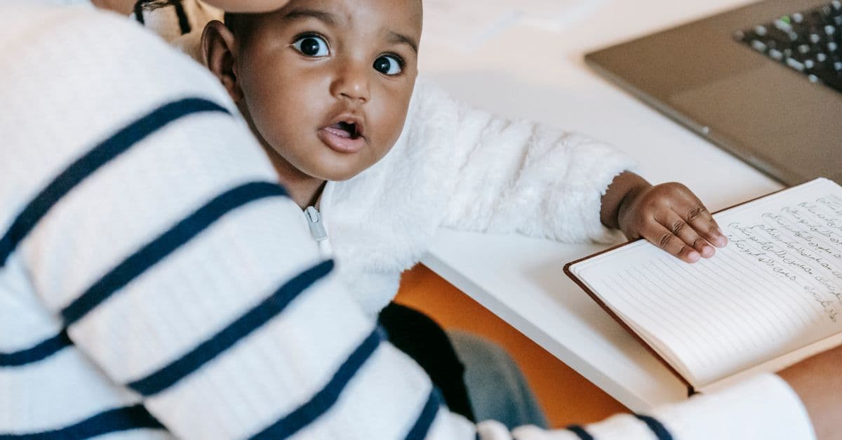 Indian child with woman in casual clothes at table with opened notepad and netbook in light flat