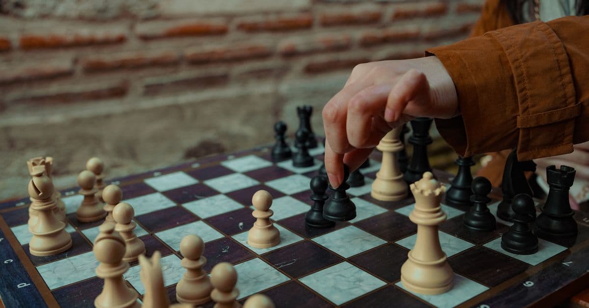 A person making a chess move on a wooden board with brick wall background.