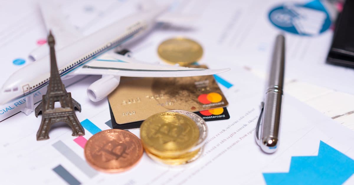 A travel finance concept featuring cryptocurrency, credit card, airplane model, and Eiffel Tower on financial documents.