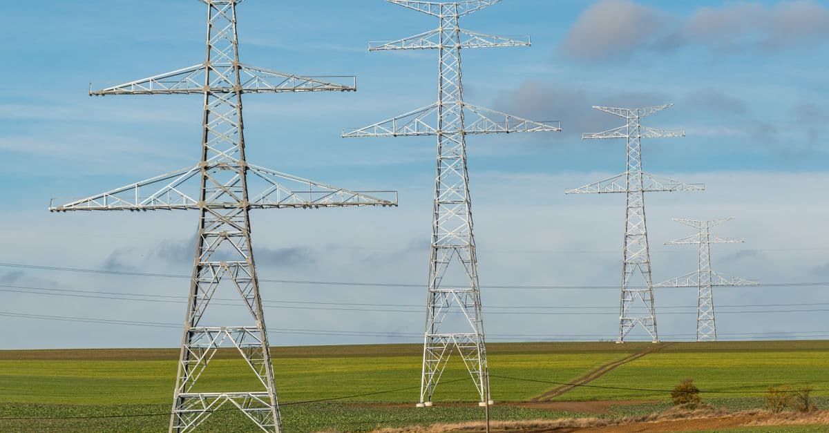 Series of transmission towers on green fields under blue skies, symbolizing energy distribution.
