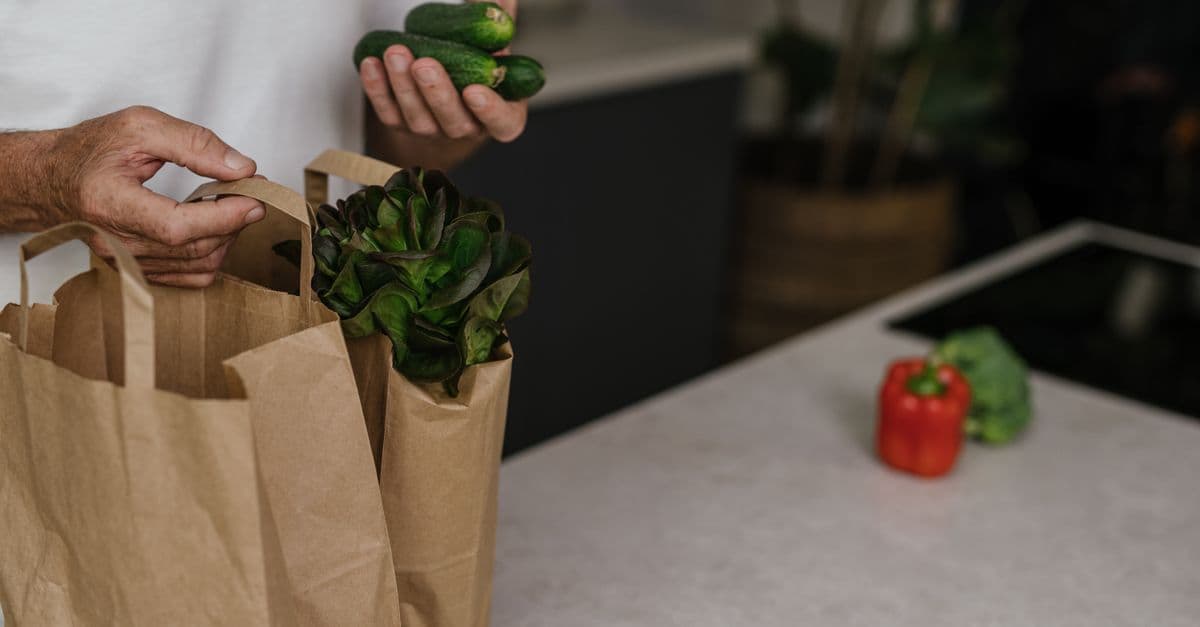 A person placing fresh vegetables into a paper bag on a kitchen counter. Vibrant and healthy organic ingredients.