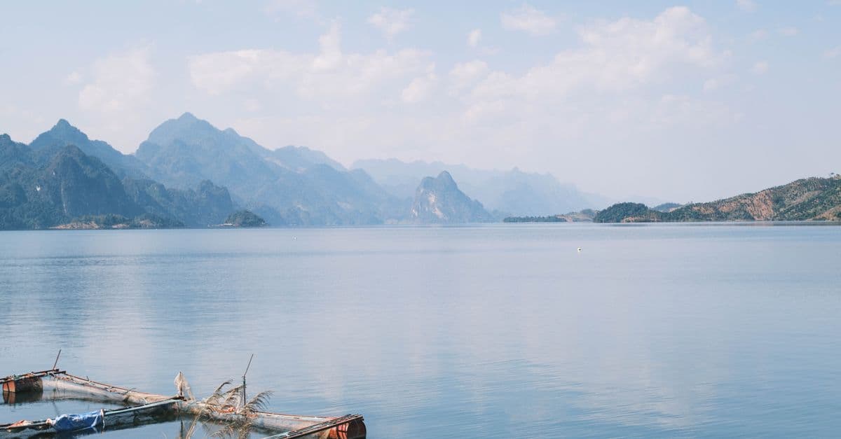 A serene mountain lake with clear blue sky and distant peaks reflecting in the calm water.