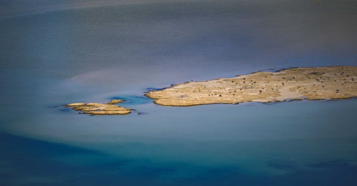 A serene aerial view of a small deserted islet in calm blue waters.