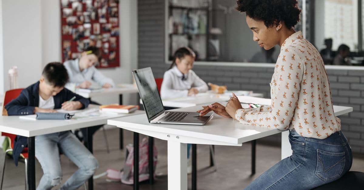 Focused teacher with students working at desks in an indoor classroom environment.