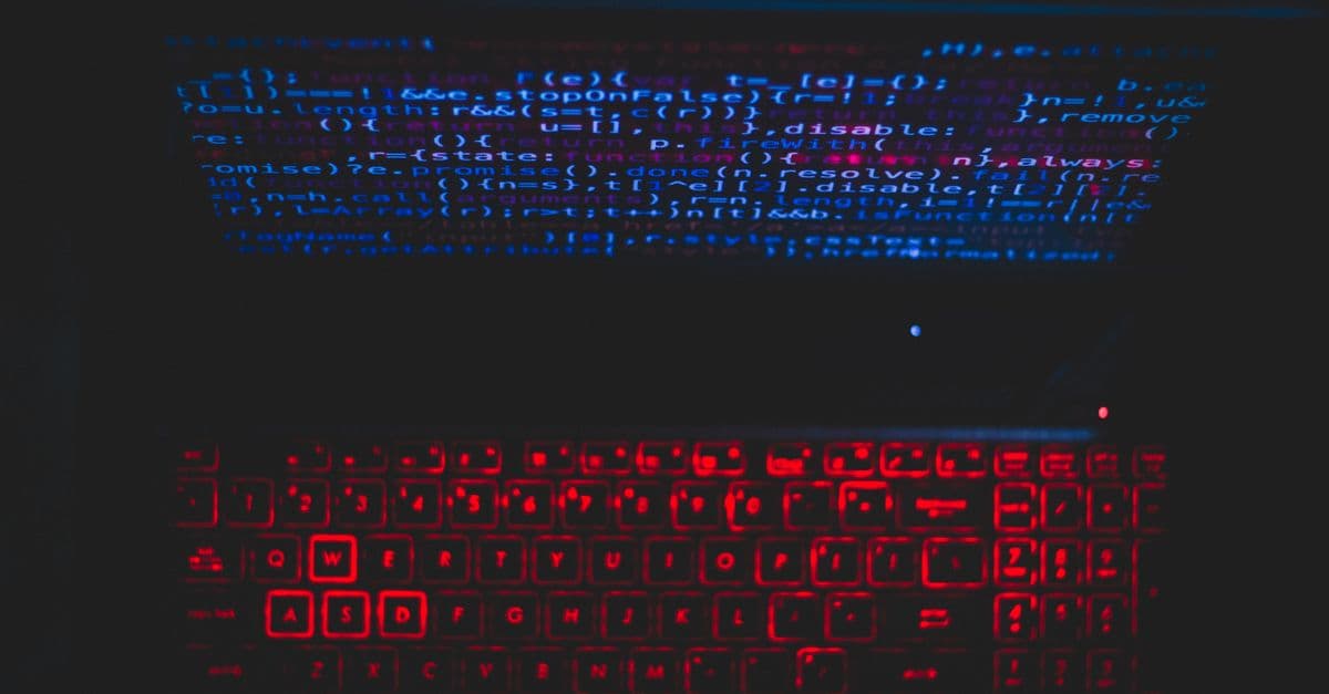 Dark-themed laptop setup with a red glowing keyboard and code on screen, ideal for tech enthusiasts.