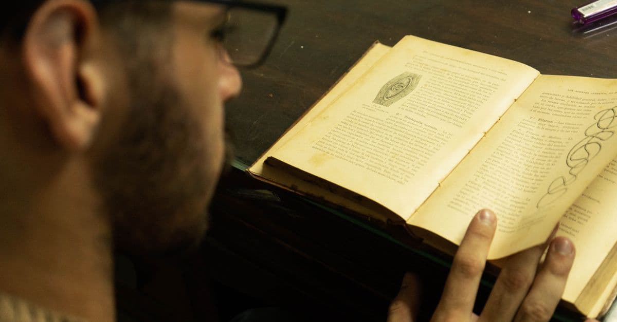 A man with glasses intensely reading an antique book indoors, capturing a study moment.