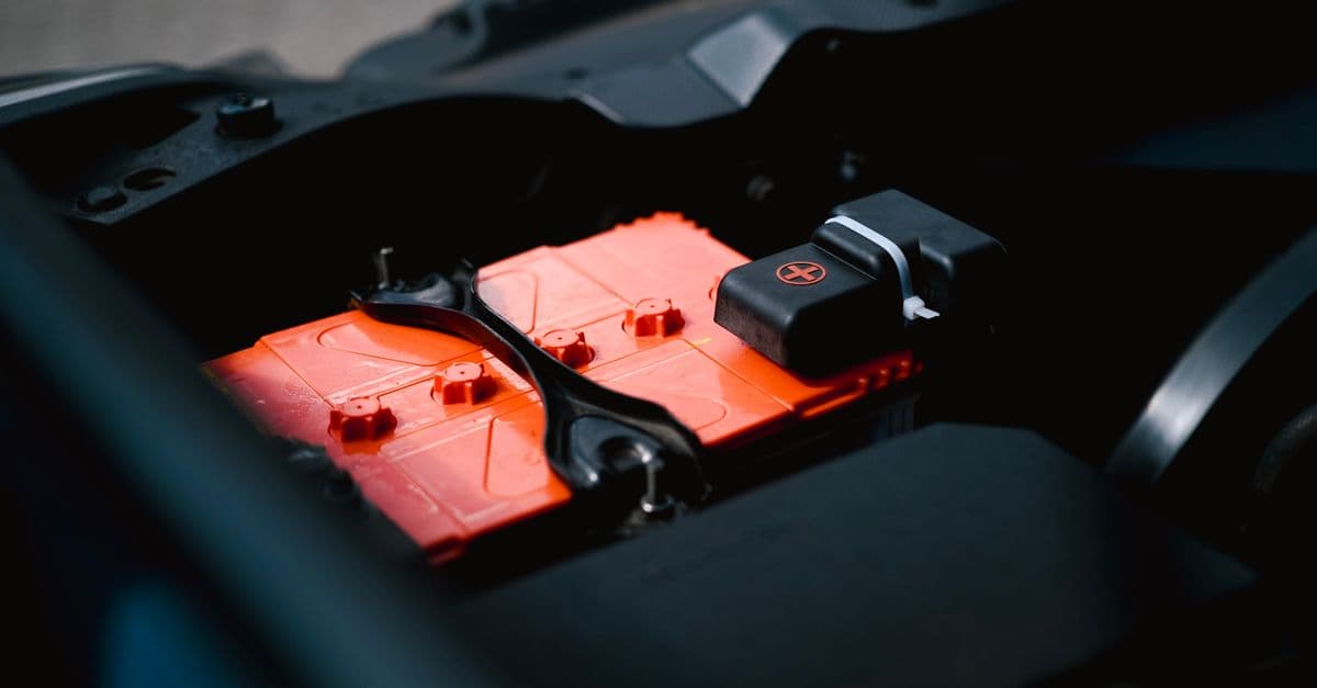 Detailed view of an orange car battery inside a vehicle's engine bay, highlighting its features.