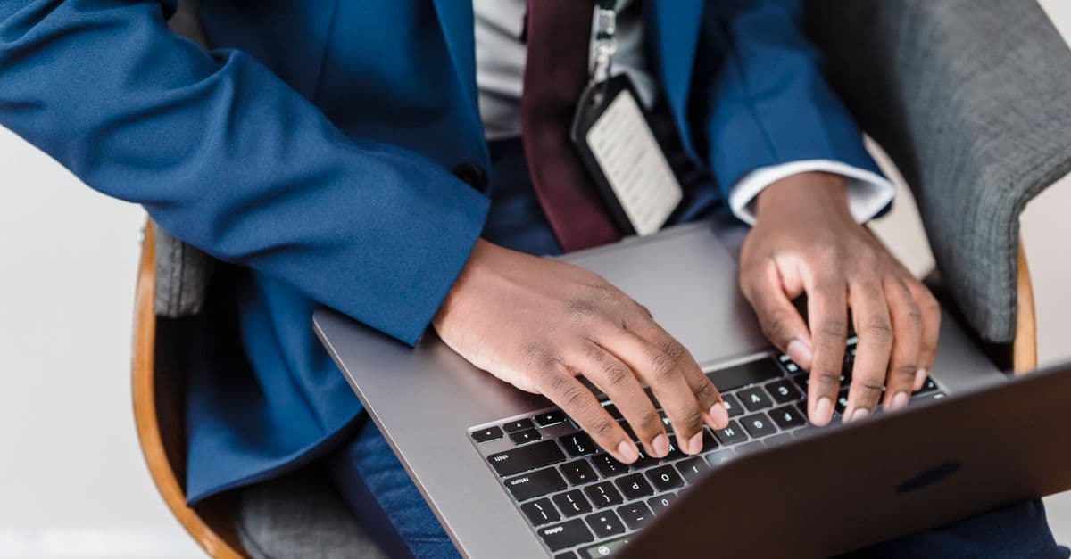 Close-up of a businessman in a blue suit working on a laptop indoors.