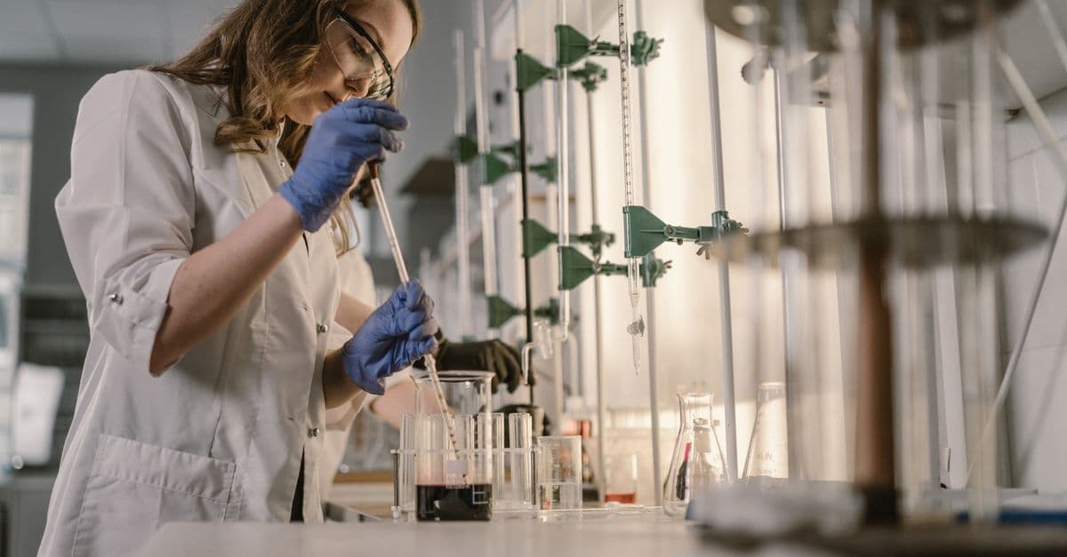 Female scientist performing an experiment in a laboratory setting with lab equipment and safety gear.