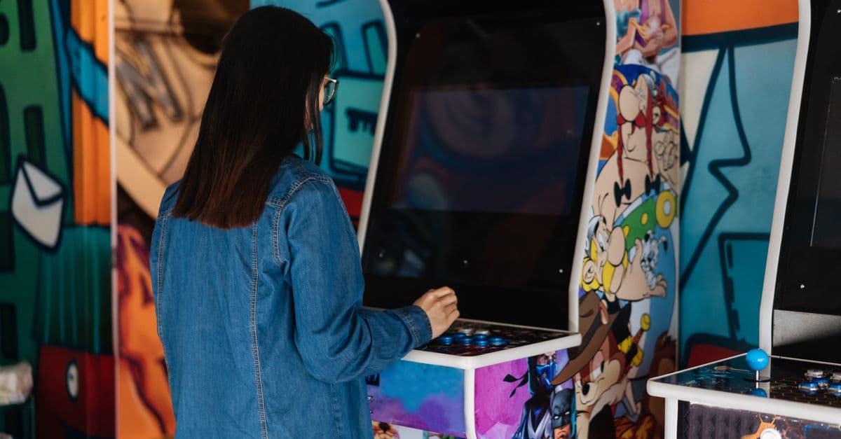 A woman with long hair plays a retro arcade game indoors, enjoying classic gaming fun.