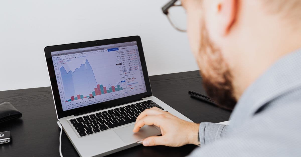 Man working on a laptop analyzing business data and financial graphs indoors.