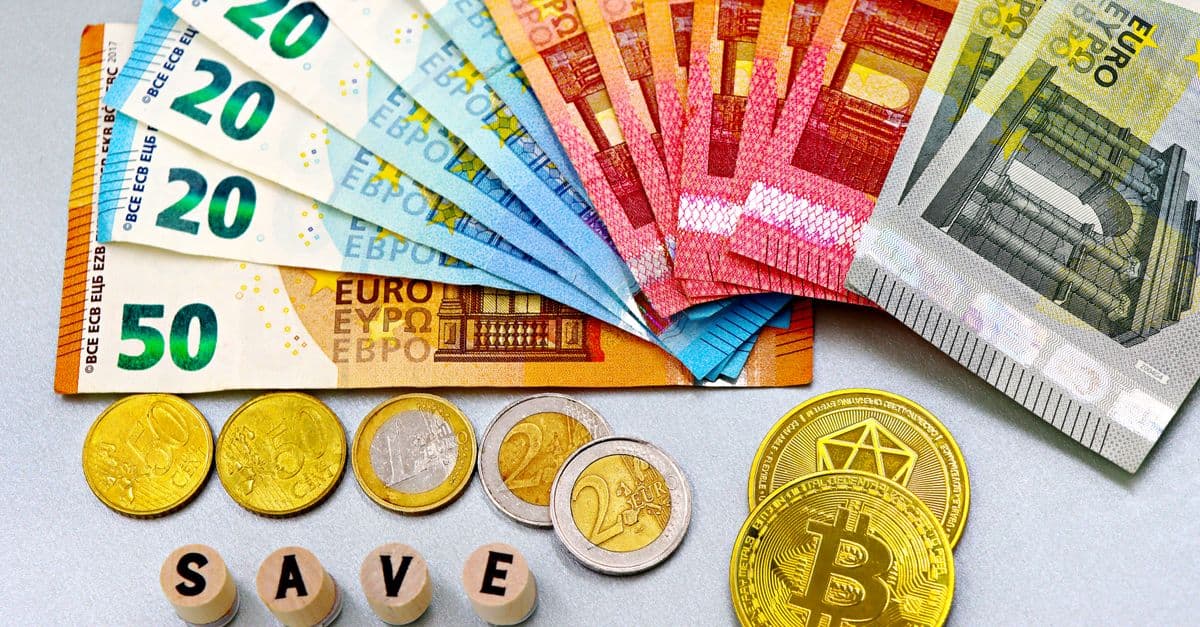 Euro banknotes and cryptocurrency coins arranged on a white surface with blocks spelling 'SAVE'.