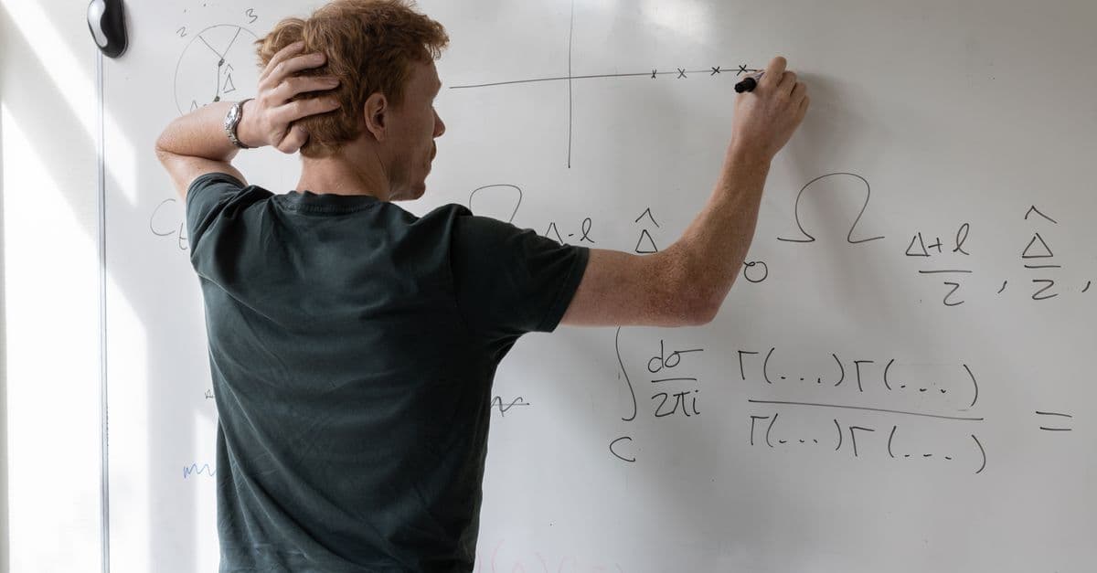 Teacher writing mathematical equations on whiteboard in a classroom setting.