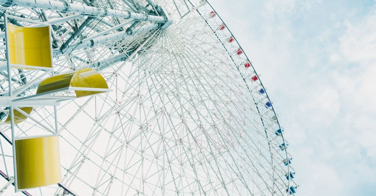 Colorful ferris wheel with yellow cabins against a bright sky, offering a fun, adventurous vibe.