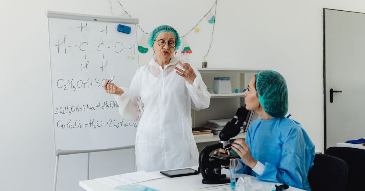 Female scientists in protective gear discussing chemical formulas in a laboratory.