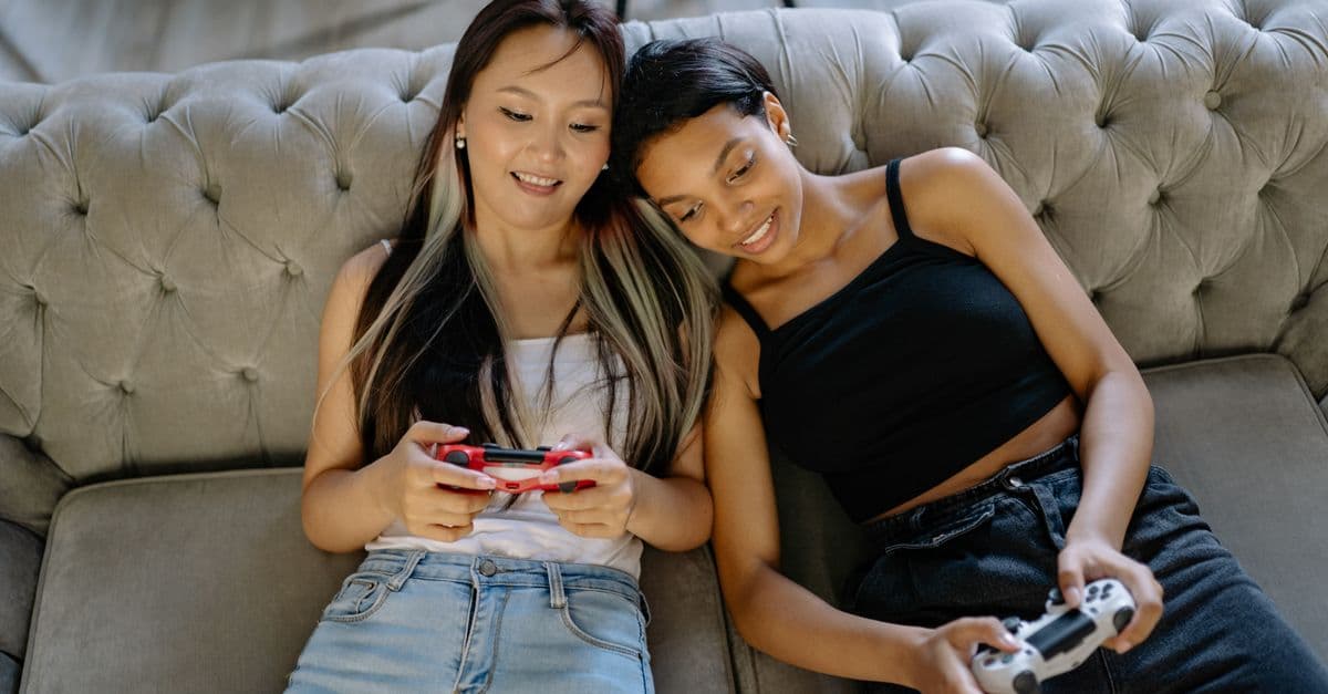 Two women relaxing and playing video games on a comfortable sofa together.