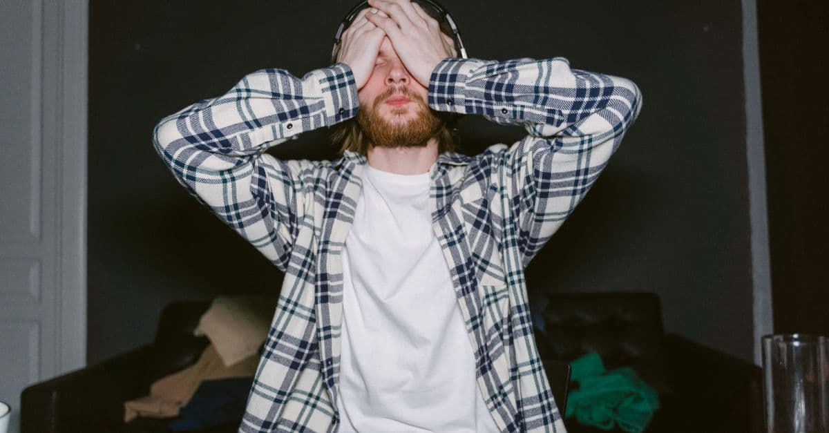 Focused male gamer in plaid shirt, showing stress with hands on face, indoors.