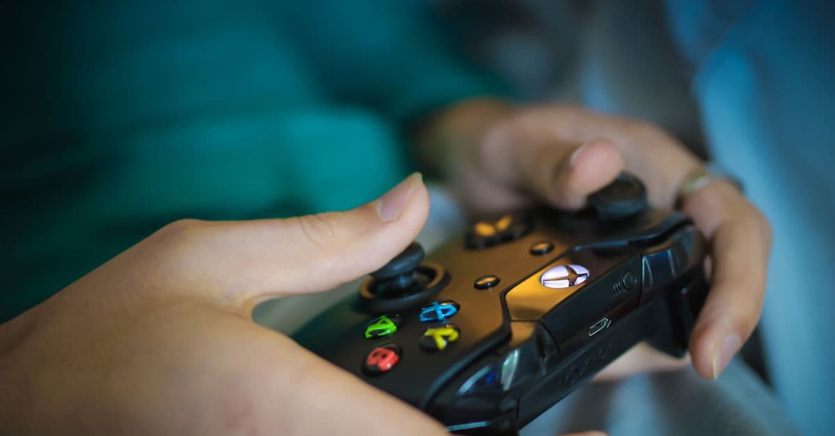 Hands gripping a modern wireless gaming controller indoors. Perfect for tech enthusiasts.