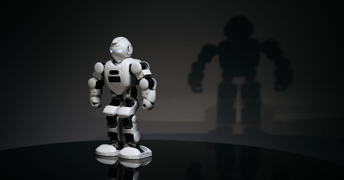 A white and black toy humanoid robot in a studio setting casting a shadow.