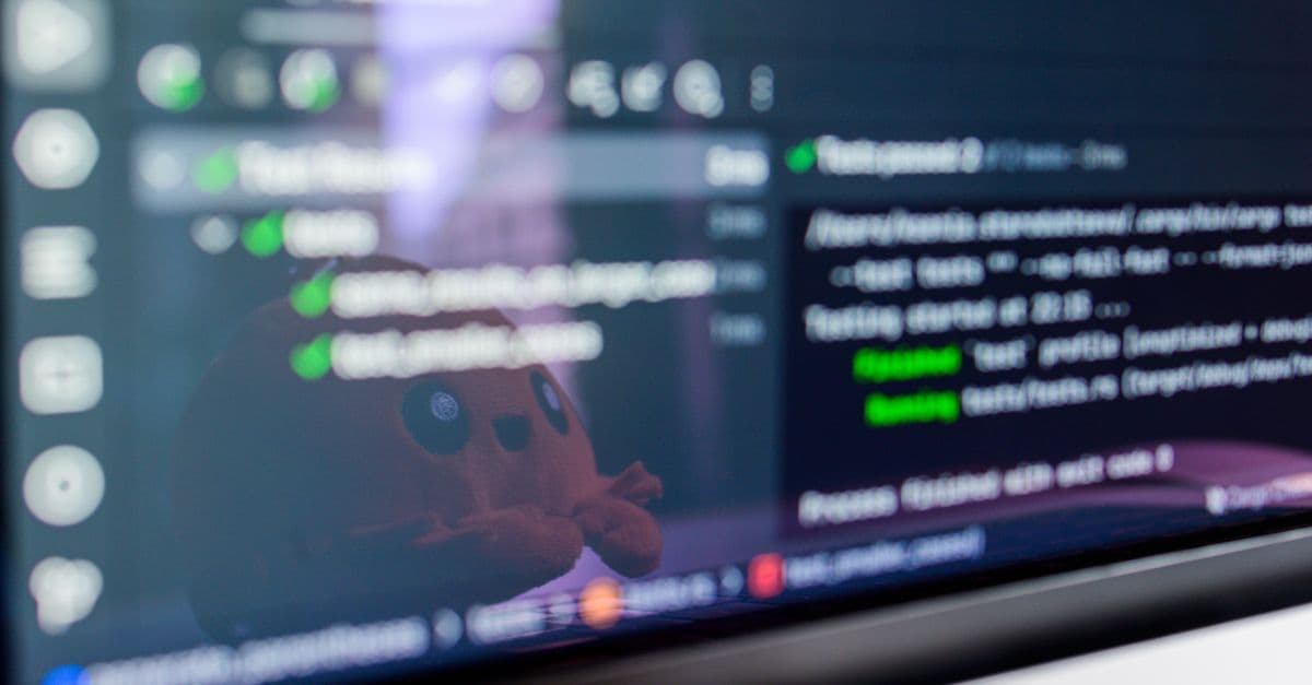 Close-up of a laptop screen displaying programming code with a cute plush toy reflecting.