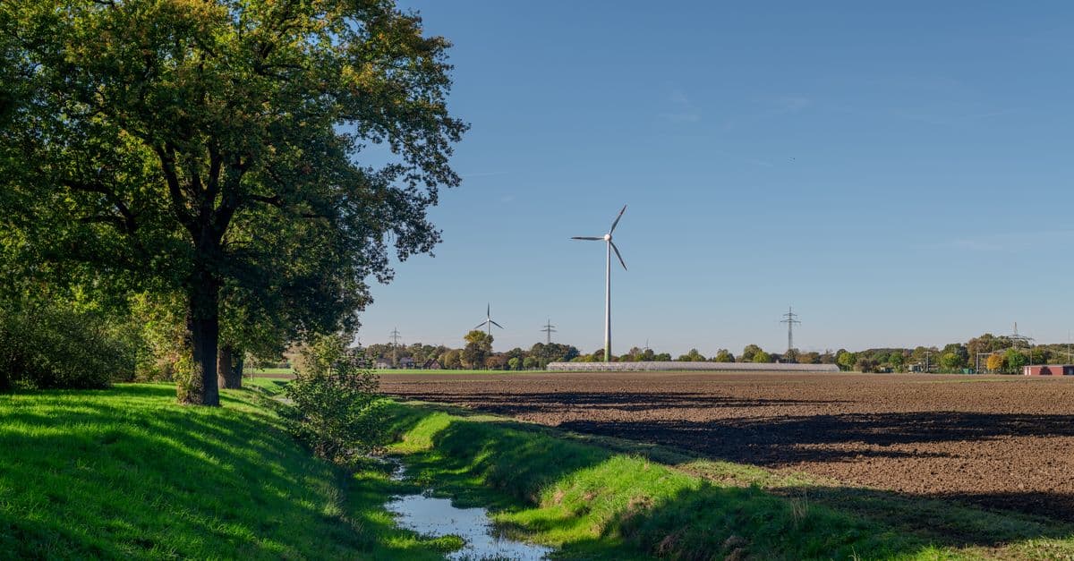 A picturesque rural landscape featuring wind turbines and green fields under a clear blue sky.