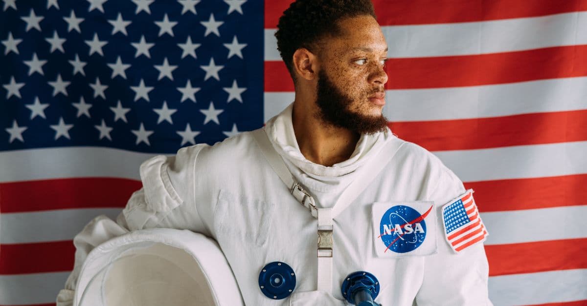 Portrait of a man in a space suit against an American flag backdrop, representing NASA.