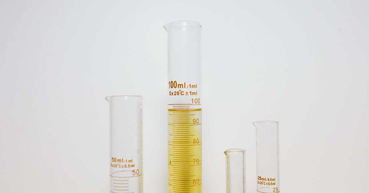 Close-up of graduated cylinders filled with yellow liquid in a laboratory setting.
